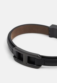 Black leather belt featuring a textured finish, dual straps, and a matte black metal buckle with an embossed logo detail.