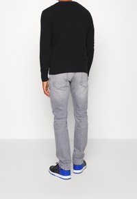 Suéter de punto negro, jeans grises con bolsillos traseros y zapatillas negras con acentos azules. Conjunto informal visto desde atrás.
