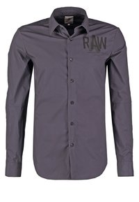 Chemise gris foncé à manches longues avec col et boutons, motif texte noir "RAW" sur la partie supérieure gauche de la poitrine.