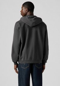 Sudadera gris oscuro con un bolsillo tipo canguro, puños acanalados y capucha adjunta. Combinada con jeans azul oscuro que presentan bordados en los bolsillos traseros.