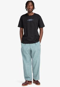 Black cotton t-shirt featuring "ELEMENT SKATEBOARD CO. WORLD WIDE" text in blue, paired with light blue baggy trousers and brown shoes.