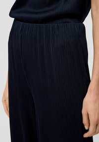 Marineblauwe geplooide broek met een elastische tailleband, voorzien van verticale ribbeltextuur en een relaxte pasvorm, getoond van de taille tot halverwege de dij.