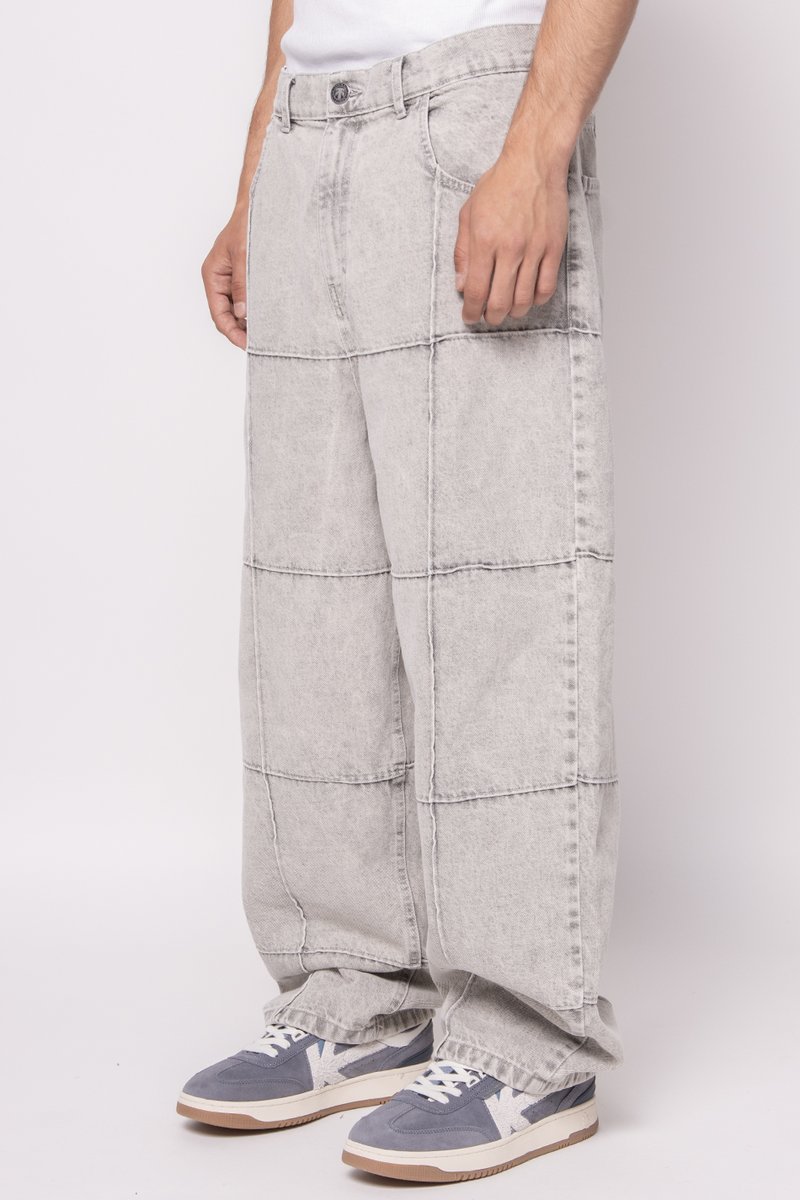 Lichtgrijze denim wijde broek met een patchworkontwerp en gestikte lijnen. Gepaard met grijs-witte sneakers voor contrast.