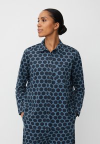 Camicia blu navy con grandi pois neri; presenta una chiusura con bottoni sul davanti, colletto e tasca sul lato sinistro del petto. Tessuto in cotone.