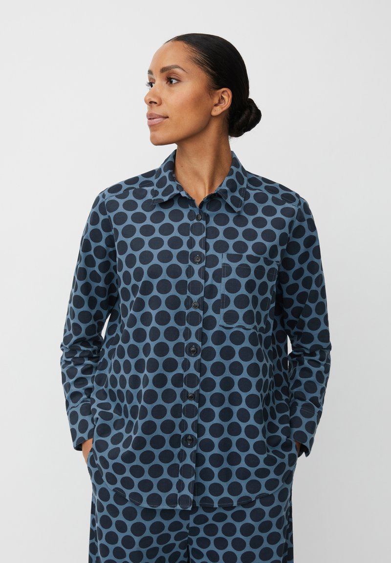 Camicia blu navy con grandi pois neri; presenta una chiusura con bottoni sul davanti, colletto e tasca sul lato sinistro del petto. Tessuto in cotone.