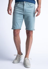 Shorts de mezclilla azul claro con dobladillos enrollados, diseño de cinco bolsillos y cierre frontal con botón, combinados con zapatillas blancas.