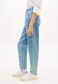 Ανοιχτό μπλε τζιν παντελόνι με ψηλή μέση και άνετη εφαρμογή. Διαθέτει φερμουάρ, πλαϊνές τσέπες και διπλωμένα τελειώματα. Φοριέται με λευκά αθλητικά παπούτσια.