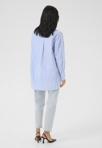 Cămașă albastră deschis cu dungi, cu mânecă lungă și croi lejer, detaliu cu pliu în spate, asortată cu blugi din denim deschis și sandale negre cu toc.