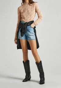 Beżowy sweter dzianinowy w pionowe wzory, niebieskie szorty dżinsowe z postrzępionym dołem oraz czarne skórzane buty kowbojskie. Czarna kurtka związana w talii.