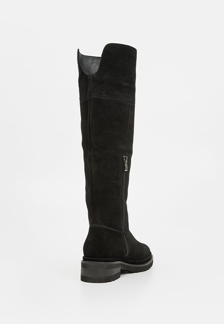 Schwarze Wildleder-Stiefel über dem Knie mit strukturiertem Finish, seitlichem Reißverschluss und breitem Absatz. Mit einer leichten Kurve am oberen Schaft.