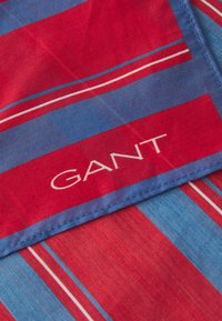 Gestreifter Baumwollstoff in Rot und Blau mit weißen Akzentstreifen. Das "GANT"-Logo ist in Weiß gestickt. Glatte Textur.