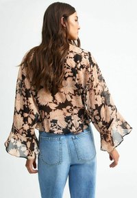 Svart blommig blus med persikofärgad mönster, genomskinligt tyg, vida trumpetärmar och en kort design, matchad med blå högmidjade jeans.