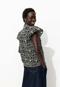 Blouse à motifs noir et blanc avec des manches volantées, un design texturé et une coupe décontractée, assortie à un pantalon en denim foncé.