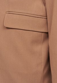 Light brown blazer featuring a textured fabric with a notch lapel and a single breast pocket. The design is tailored and structured.