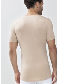 Camicia beige a maniche corte realizzata in tessuto morbido, design aderente con scollatura rotonda e dettaglio di cucitura minimalistico sul retro.