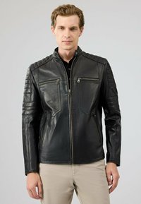 Zwarte leren jas met een getailleerd ontwerp, voorzien van gestikte schouderaccenten en twee ritszakken aan de voorkant. Glad textuur, elegante stiksels.