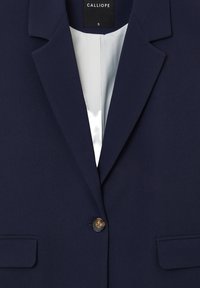 Blazer bleu marine avec une fermeture à bouton unique, un col à revers cranté et deux poches avant. Doublure intérieure en satin lisse.