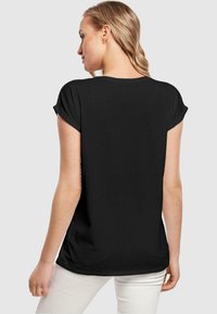 Sort kortærmet t-shirt med rullemanchetter, afslappet pasform og glat tekstur, vist bagfra, parret med lyse bukser.