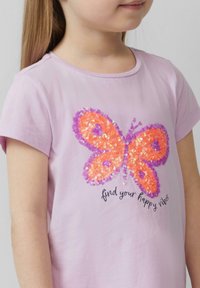 Lichtpaarse katoenen t-shirt met een vlinderontwerp gemaakt van oranje en paarse pailletten, met de tekst "vind je gelukkige vibes" eronder.