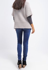 Poncho gris clair en maille avec manches courtes, associé à un jean bleu ajusté et des bottines noires à talon épais.
