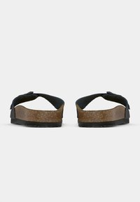 Sandales en liège marron avec des brides noires vues de dos sur un fond blanc uni.