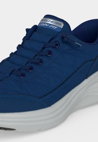 Μπλε αθλητικό παπούτσι Skechers Cozy Fit με επάνω μέρος από υφασμάτινο καπιτονέ, σκούρα μπλε κορδόνια και παχύ άσπρο επενδυμένο πάτο.