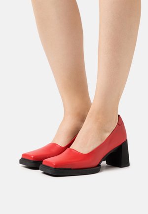 Chaussures à talons bloc rouges en cuir, avec un bout rond, présentant une texture lisse et une semelle en caoutchouc noir contrastante pour une meilleure adhérence.