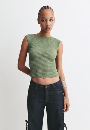 Groene cropped top met een gestructureerd, geribbeld design en korte mouwen, gecombineerd met donkere denim jeans met een aansluitende taille en zijkanten met strikjes.