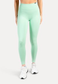 Mintgröna leggings med hög midja, slät textur och figurnära siluett, kombinerade med vita träningsskor.