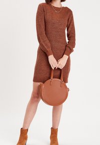 Robe en tricot marron à manches longues et décolleté en V, associée à un sac à main rond beige avec une surface texturée et des poignées doubles.