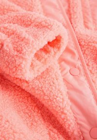 Rózsaszín, bolyhos dzseki puha, texturált anyagból, bolyhos külsővel és sima béléssel, patentos záródással.