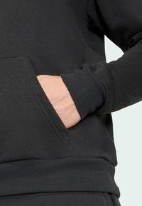 Haut noir à capuche avec une poche kangourou, des poignets et un ourlet côtelés. Le tissu semble doux avec une texture lisse.