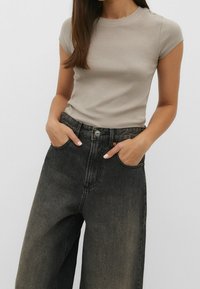 Beige short-sleeve t-shirt paired with black high-waisted wide-leg jeans, featuring a faded texture and front pockets.