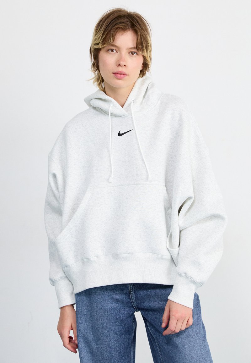 Svijetlosiva dukserica s džepom sprijeda, elastičnim manžetama i malim crnim Nike logom na prsima. Teksturalna tkanina i širok kroj.