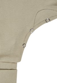 Beiger, gerippter Strickstoff mit drei silbernen Druckknöpfen entlang einer geschwungenen Kante, neben einem gefalteten Bündchen.