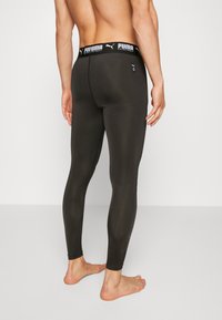 Leggings sportivi neri con design aderente, vita elastica con logo PUMA e texture liscia. La vista posteriore mette in mostra la forma delle gambe.