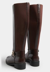 Bruna knähöga stövlar med läder- och nätpaneler, en slät yta, en lätt klack och en dekorativ spänne på ankelremmen.