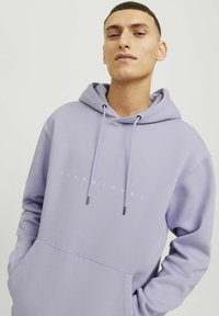 Šviesiai purpurinė hoodie su kengūros kišene, raišteliais su metaliniais antgaliais ir balta logotipu priekyje. Lygus audinio paviršius.