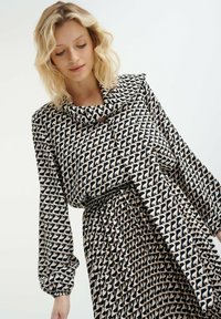 Zwarte en beige gebloemde blouse met een gedrapeerde halslijn, lange pofmouwen en een bijpassende gerimpelde rok met hetzelfde geometrische ontwerp.