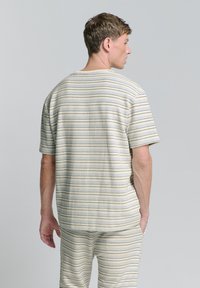 Korte mouwen, textured top in beige met horizontale strepen in blauw en groen. Relaxte pasvorm, ronde halslijn en bijpassende, gestreepte broek.