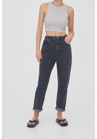 Débardeur gris court avec un col rond associé à un jean en denim noir taille haute. Le jean présente des ourlets retroussés et des poches avant. Tongs noires.