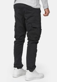 Schwarze Cargo-Hosen aus strapazierf�ähigem Baumwoll-Mix, mit mehreren seitlichen Taschen, schmal zulaufenden Beinen und einer glatten Textur. Kombiniert mit weißen Sneakern.