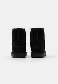 Stivali neri alla caviglia in suede. Presentano una suola in gomma piatta e dettagli cuciti. Il logo è impresso sul retro.