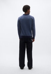 Πλεκτό πουλόβερ σε ναυτικό μπλε με διακοσμητικό μοτίβο, μανσέτες και τελείωμα με ριμπ ύφανση, συνδυασμένο με σκούρο τζιν παντελόνι. Θέα από πίσω.