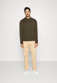 Olive green long-sleeve polo shirt with a collar and three buttons, paired with light beige chinos and white sneakers.