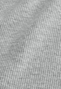 Tissu en maille côtelée gris clair avec des lignes verticales et de douces plis créant des ombres légères et une texture délicate.