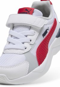 Baskets blanches en matériaux mesh et synthétiques, avec des accents rouges et gris, une sangle Velcro et des panneaux latéraux texturés.