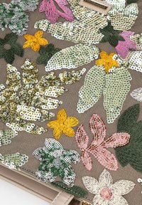 Sac brodé avec des motifs floraux multicolores en sequins et en fil sur un fond texturé beige.