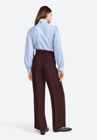 Lichtblauw geblokt blouse met puffmouwen en een kraag, gecombineerd met hoge donkere bruine wijde broek. Beschikt over een achterzak.