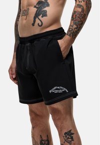Zwarte shorts met een elastische tailleband, contrasterende stiksels, zijzakken en witte logodetails. Gemaakt van een lichtgewicht stof.
